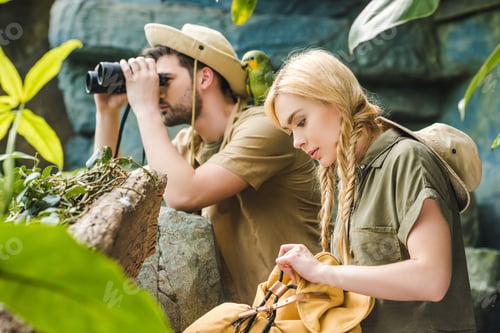 Preview: active young couple in safari suits with parrot hiking in jungle