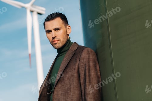 Preview: A man in a business suit with a green Golf shirt stands next to a windmill against the background of