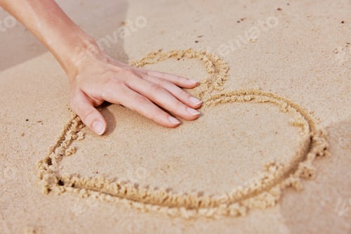 Preview: Hand drawing heart in sand on beach with word love written next to it
