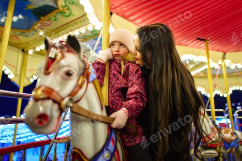 Preview: Joyful mother and daughter share a moment on a carousel at night