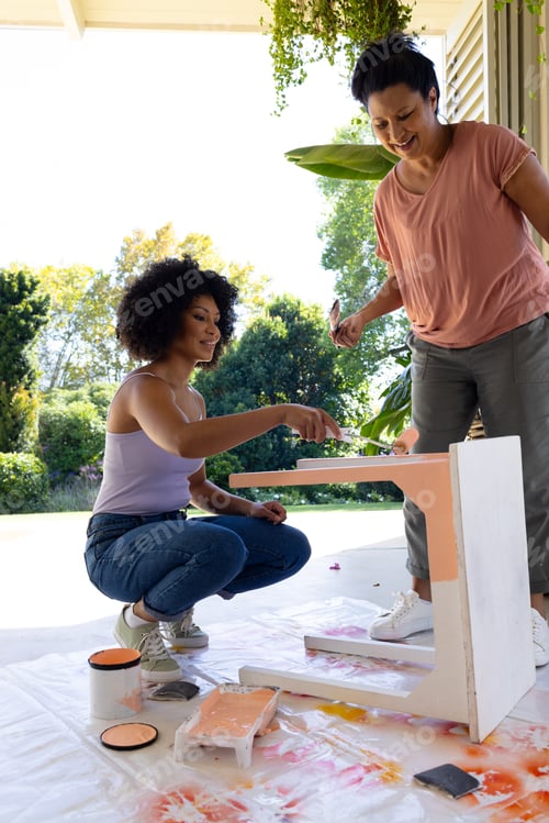Preview: Biracial mother and adult daughter painting furniture outdoors at home in an upcycling project