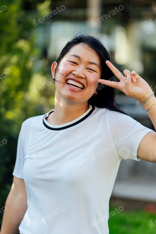 Preview: Smiling asian woman gesturing peace sign