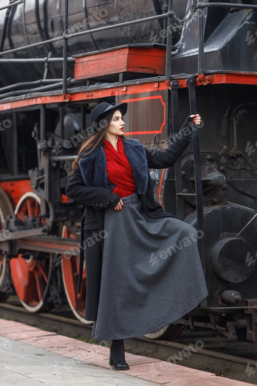 Preview: A girl in a black coat and hat on the running board of an old steam locomotive. Vintage portrait