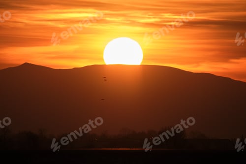 Preview: Beautiful evening panoramic landscape with bright setting sun over distant mountain