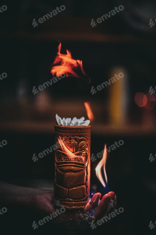 Preview: Vertical shot of a burning cocktail in a tiki cup on a bratender's hand.