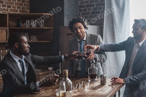 Preview: smiling multiethnic male friends clinking glasses of whiskey and partying together