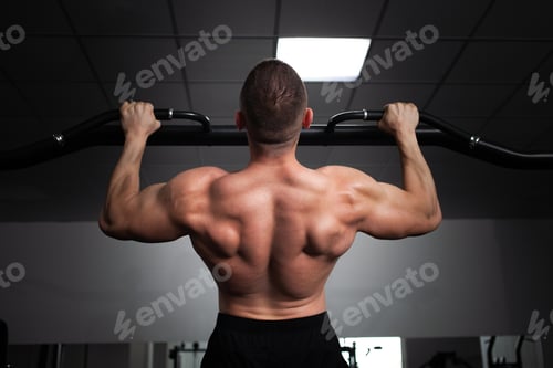 Preview: A man athlete bodybuilder pulls up on his hands, builds muscles, does an exercise in gym. back