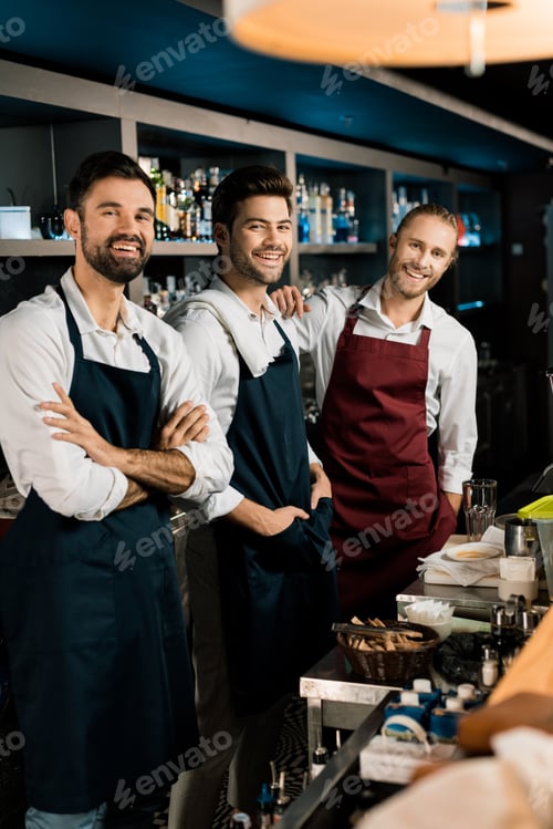 Preview: Handsome bartenders standing in aprons and smiling in bar