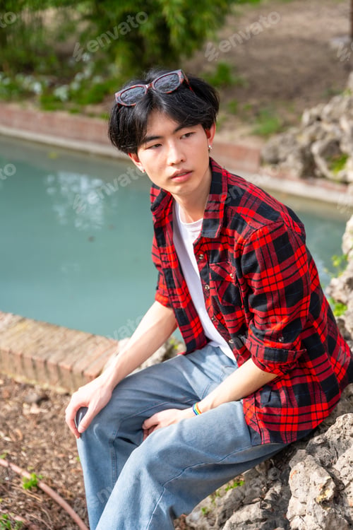 Preview: Asian gay man sitting next to urban park with water