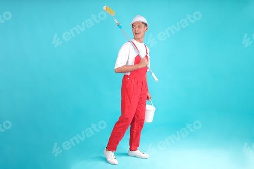 Preview: Full Body Young Employee Laborer Handyman Stand with Roller Brush and Bucket on Blue Background