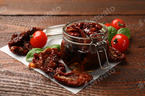 Preview: Delicious sun dried tomatoes in glass jar, fresh vegetables and basil on wooden table, closeup