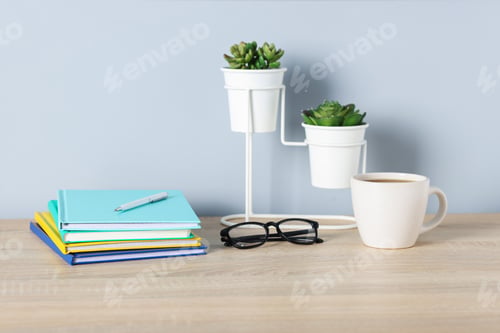 Preview: Different stationery, glasses, coffee and floral decor on wooden office table near light wall