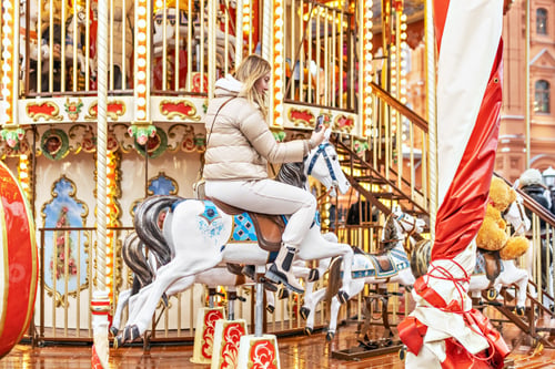 Preview: Children's carousel with horses at the Christmas market. A young blonde woman rides a horse