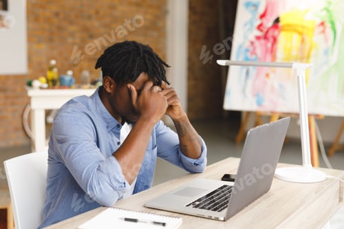 Preview: Tired african american male painter at work using laptop in art studio