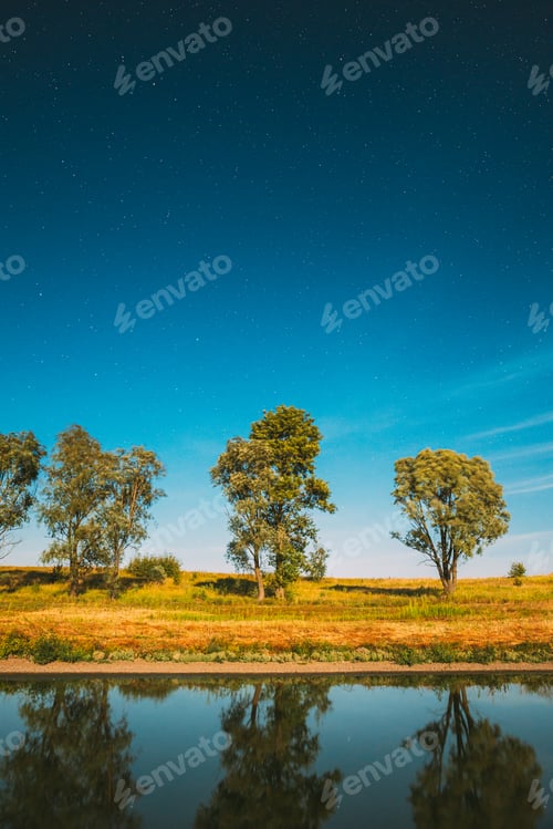 Preview: Blue Night Starry Sky Above Lake River. Night Glowing Stars And Trees Woods Reflected In Water