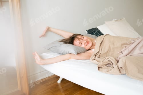 Preview: Young beautiful caucasian woman wakes up in the morning. Woman is basking in her bed.