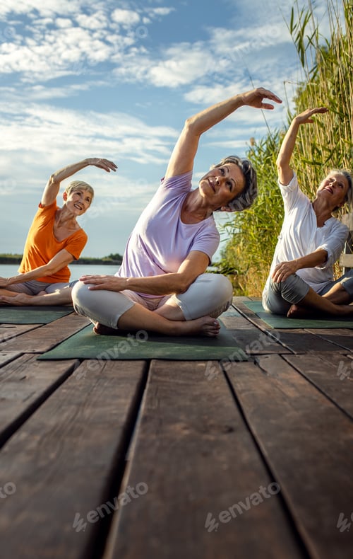 Preview: Group of senior woman doing yoga exercises by the lake.