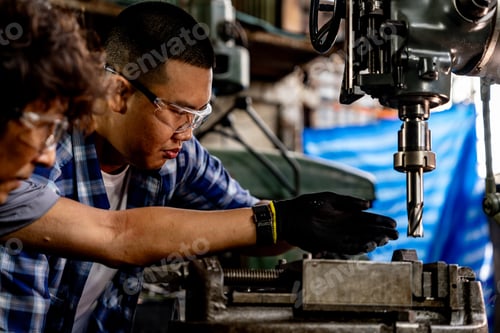 Preview: Asian worker in production plant drilling at machine.