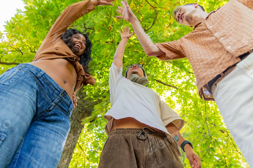 Preview: Happy Multicultural friends giving high five under green tree in park