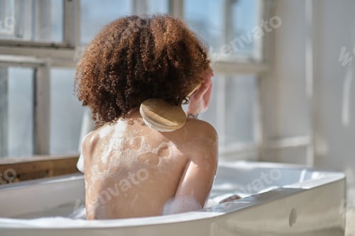Preview: Smiling and relaxing african american woman bathing in a tub full of foam.