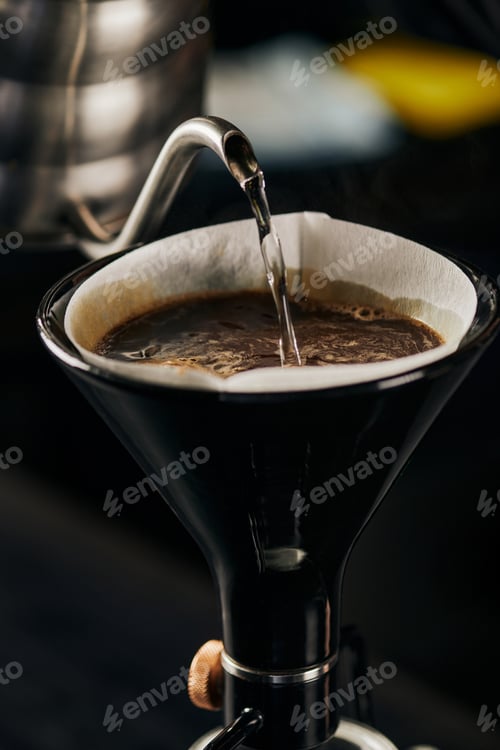 Preview: boiling water pouring from kettle into siphon coffee maker with paper filter and coffee with foam