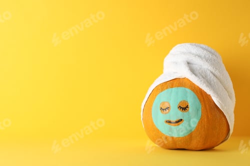 Preview: Pumpkin with facial mask and towel on yellow background, copy space