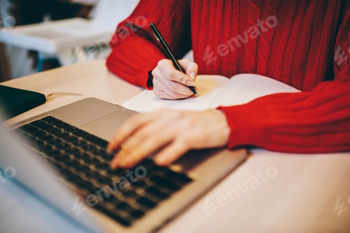 Preview: Crop freelancer taking notes from laptop in cafe