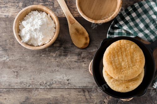 Preview: Delicious arepas in frying pan with precooked corn flour on rustic wooden table