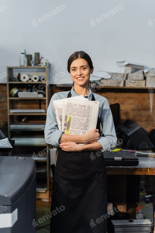 Preview: overjoyed typographer in apron holding freshly printed newspapers