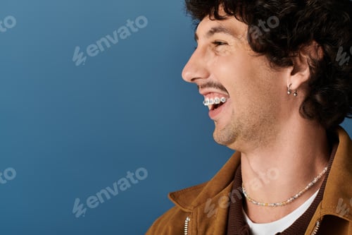 Preview: Handsome man laughing against a vibrant blue backdrop, showcasing stylish casual fashion choices