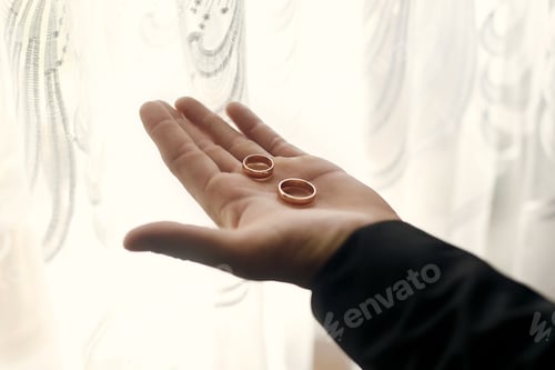 Preview: person hand holding golden wedding rings on palm in morning light at window