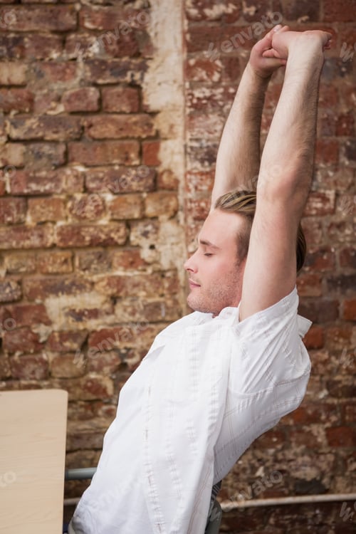 Preview: Man sitting with arms raised at desk in the office