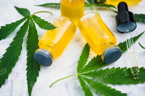 Preview: Cannabis oil in the vials with dropper tube and green leaves on marble table.
