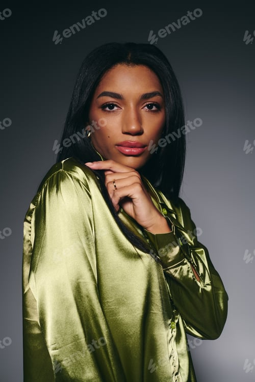 Preview: Stunning young woman in a green silk shirt poses elegantly in a modern studio setting