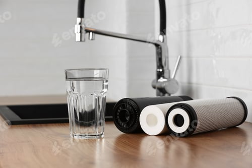 Preview: A glass of clean fresh water and set of filter cartridges on wooden table in a kitchen interior.