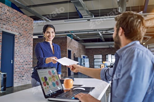 Preview: Shot of a young designer handing over paperwork to a colleague in an office