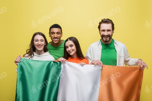 Preview: Positive multiethnic people holding Irish flag isolated on yellow