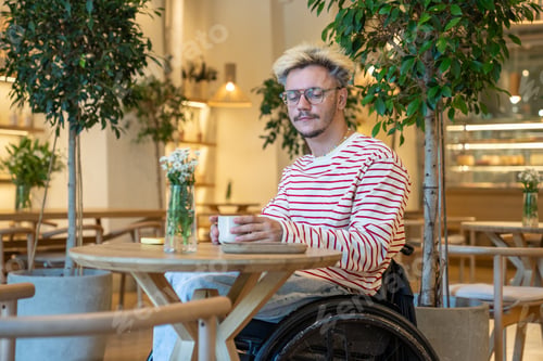 Preview: Alone thoughtful disabled young man on wheelchair spending time in cafe drinking coffee reflects.
