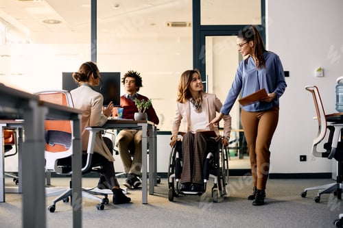 Preview: Happy businesswoman in wheelchair and her colleague talking while going through the office.