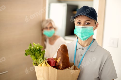 Preview: Female courier with face mask doing home delivery during COVID-19 epidemic.