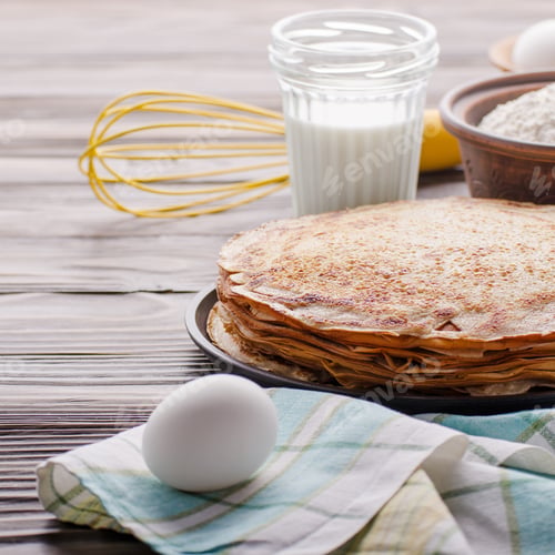 Preview: Stack of French crepes in frying pan on wooden kitchen table wit