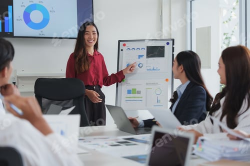 Preview: Asian businesswoman leading meeting and pointing at charts on whiteboard