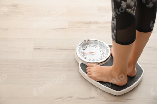 Preview: Woman measuring her weight using scales on wooden floor. Healthy diet