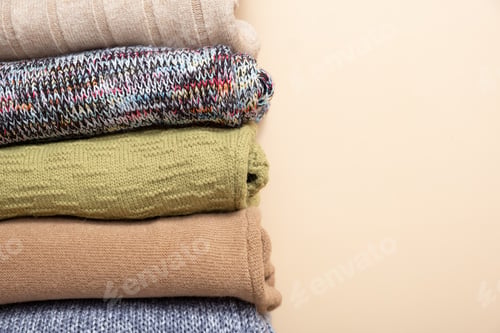 Preview: A stack of cozy knitted sweaters on beige background. Warm concept
