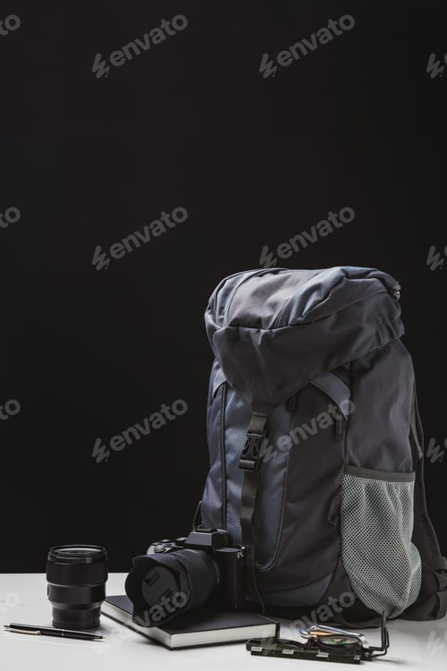Preview: backpack, photo camera with lens, notebook and trekking equipment on black