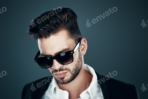 Preview: Charming young man in eyewear looking down while standing against grey background