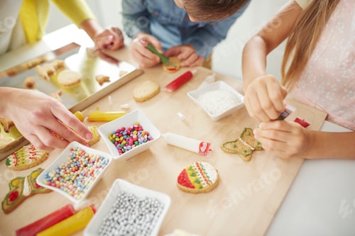 Preview: Hands of boy, his sister and mother decorating easter biscuits at kitchen counter