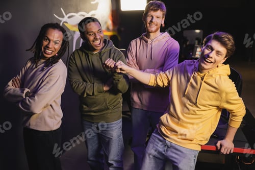Preview: Excited interracial friends looking at camera and gesturing in gaming club