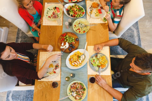 Preview: Overhead view of caucasian parents with son and daughter sitting at table and having dinner