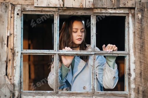 Preview: girl looks out the window from an old wooden house